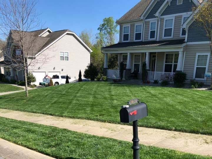 Mowed lawn with dark green stripes and a black mailbox on a post in front of a tan two-story home